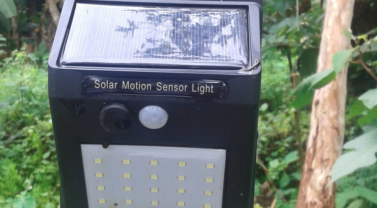 Lampe solaire murale à détecteur de mouvement : panneau sur le dessus, œil du capteur au centre, dalle de LED en bas