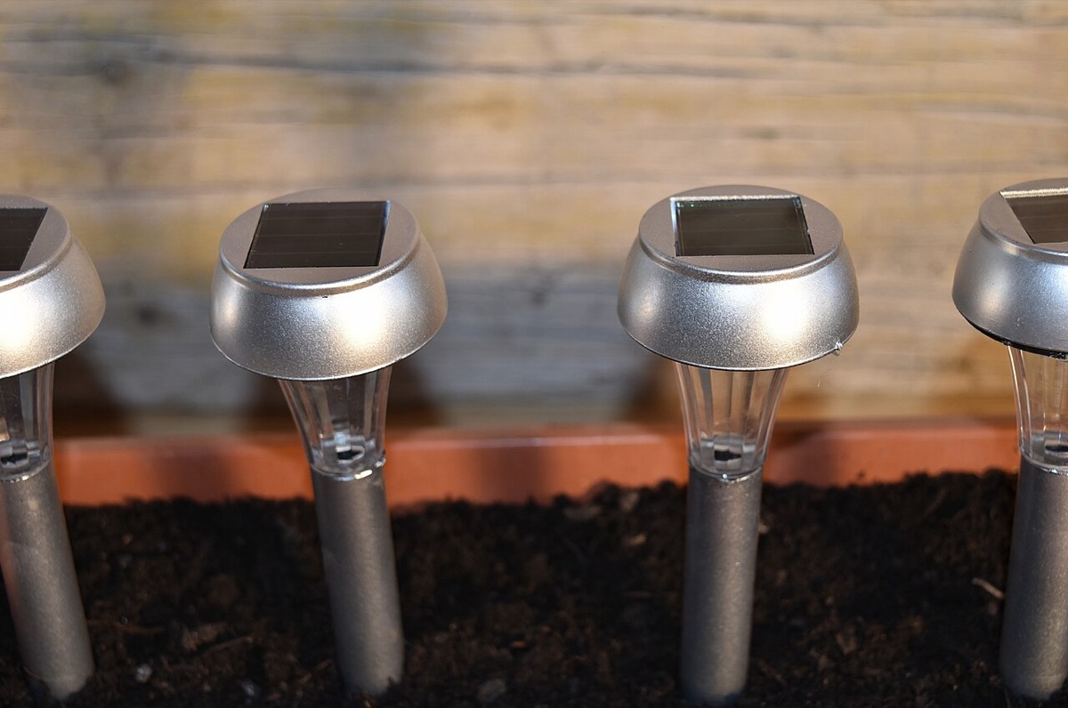 Balise solaire à piquer coiffée d'une petite cellule photovoltaïque, plantée dans un massif de jardin