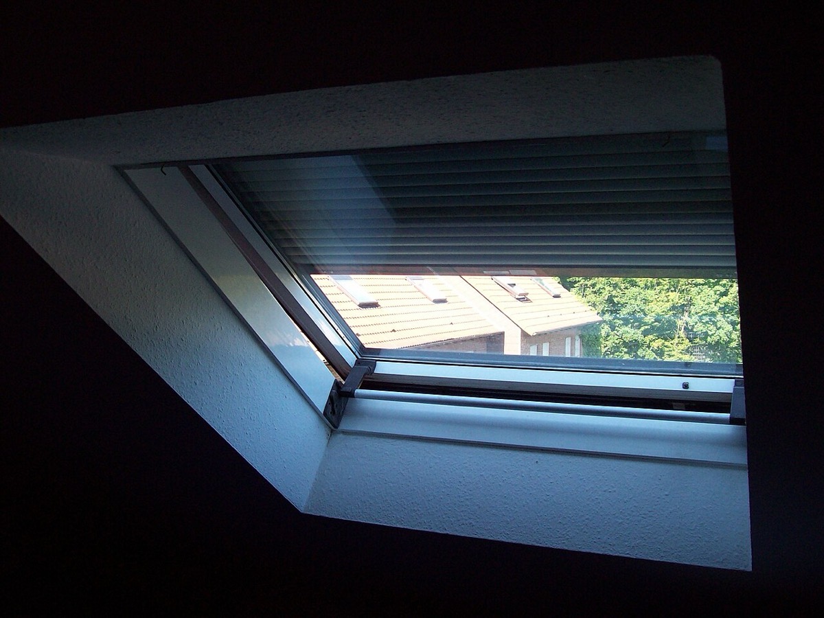 Un volet roulant à moitié descendu sur une fenêtre de toit, vu depuis l'intérieur